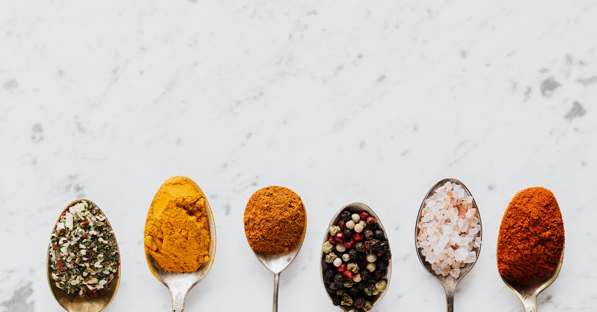 Top view of assorted aromatic condiments arranged together in metal spoons on marble surface used for delicious gourmet meal cooking