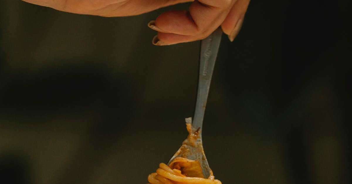 Crop faceless female using fork while eating yummy spaghetti alla bolognese during dinner in restaurant