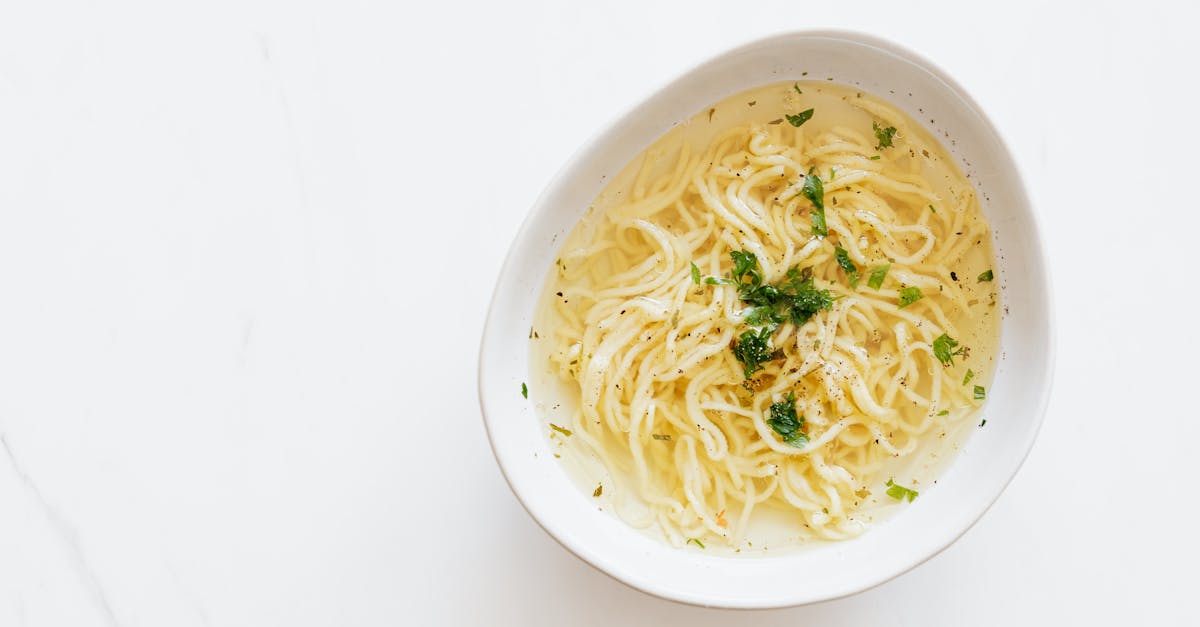 Top view of white bowl with yummy homemade noodles cooked in fresh delicious chicken broth and topped with green aromatic parsley placed on white marble table