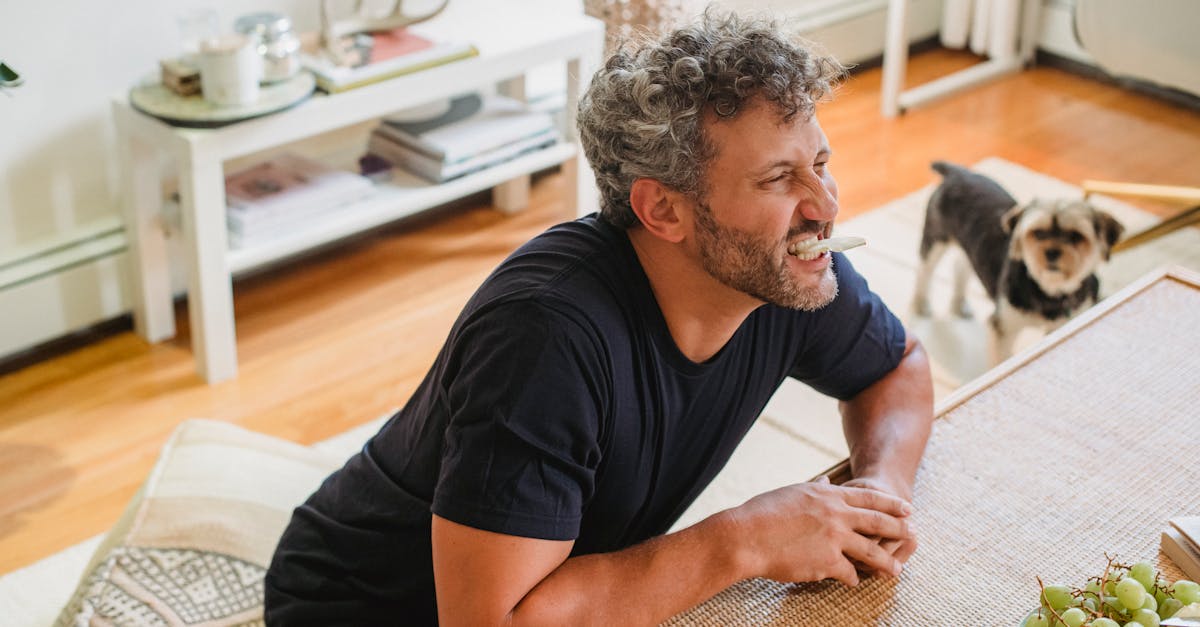 Cheerful adult male with beard and grey curly hair making faces with piece of apple in teeth