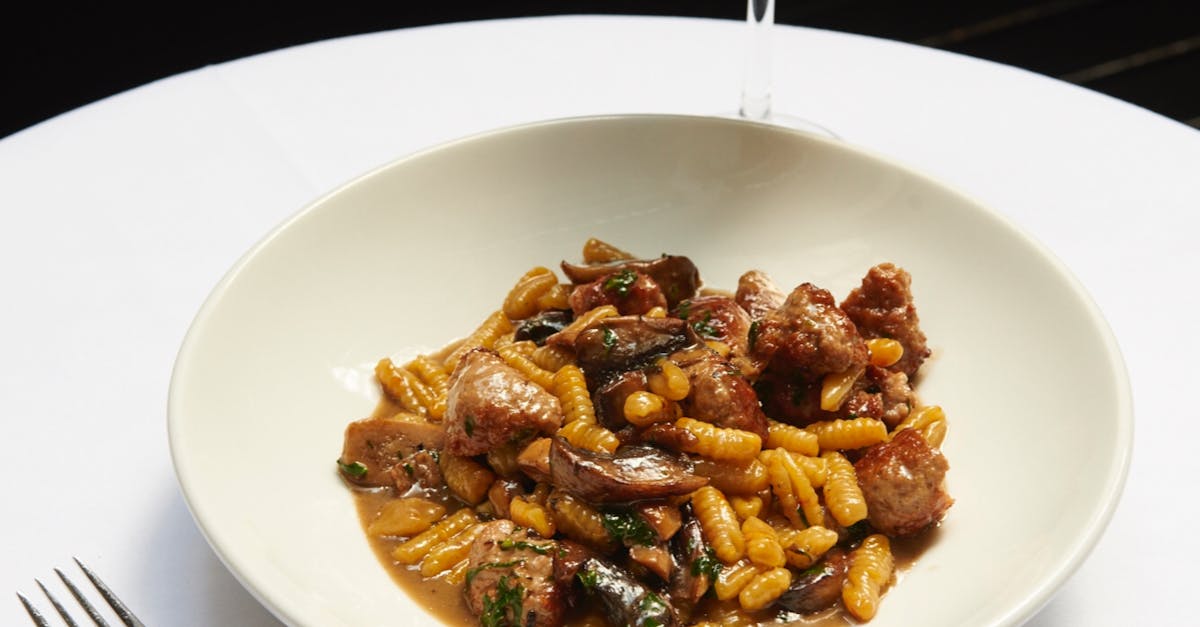 From above of palatable dish with gnocchi pasta and meat in sauce served in white ceramic plate and placed on round table with glass of wine in restaurant