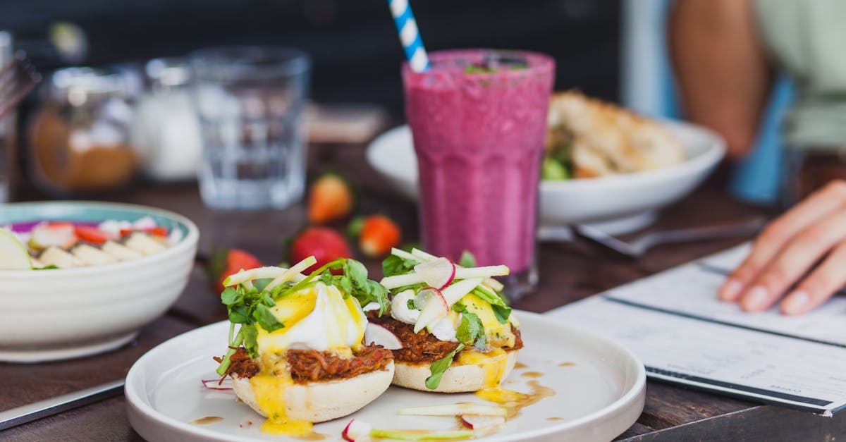 Appetizing sandwiches with poached eggs and sauce served with berry smoothie and placed on table with crop unrecognizable woman reading menu on background