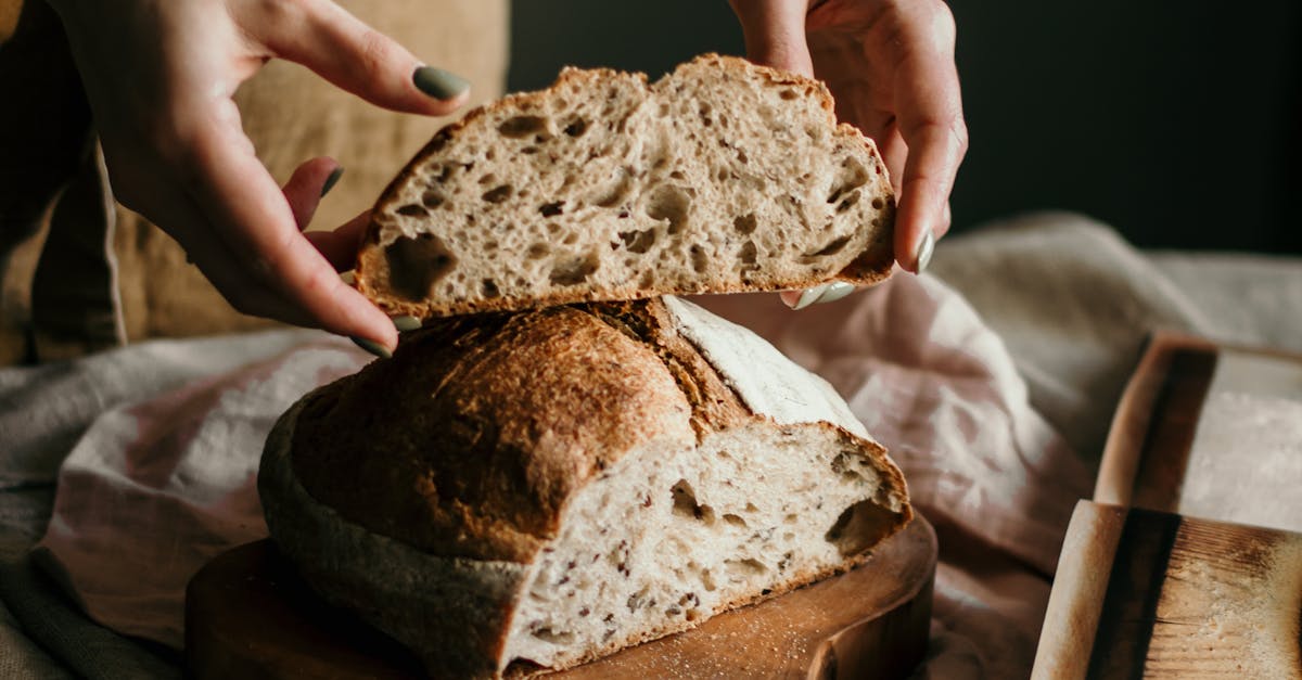 High angle of crop anonymous female baker in apron with piece of bread made with recipe from book at home