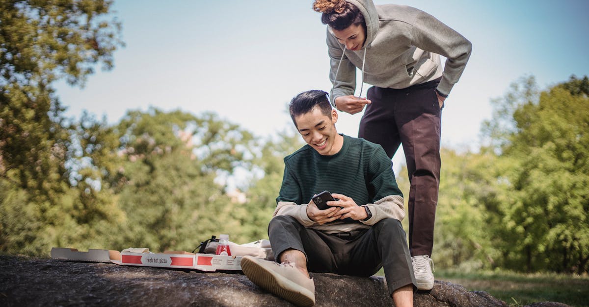 Cheerful multiethnic friends browsing smartphone while having picnic