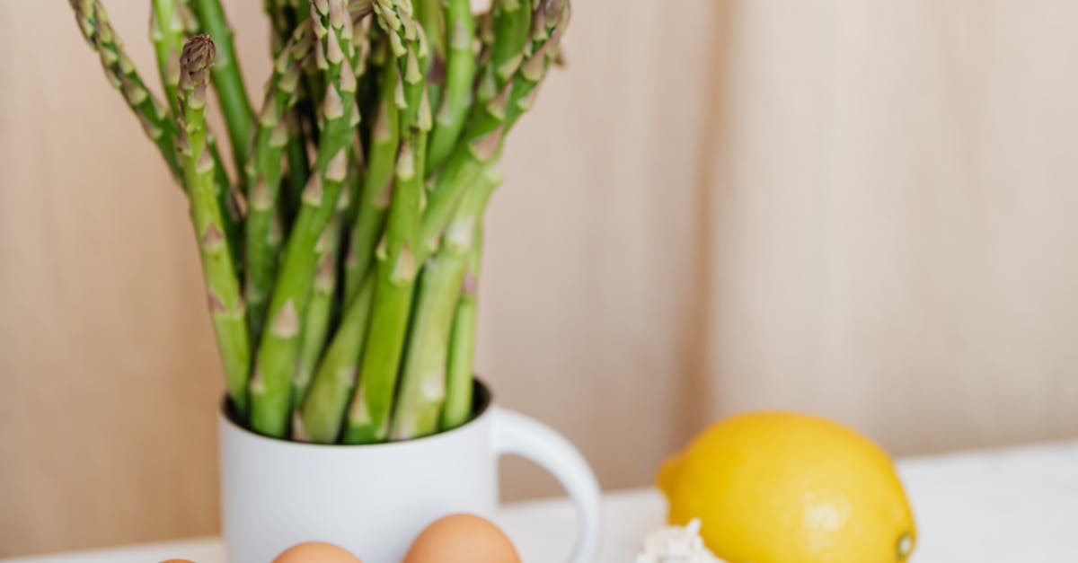 Bunch of red cherry tomatoes arranged before green asparagus and yellow lemon near garlics and metal basket with eggs on table