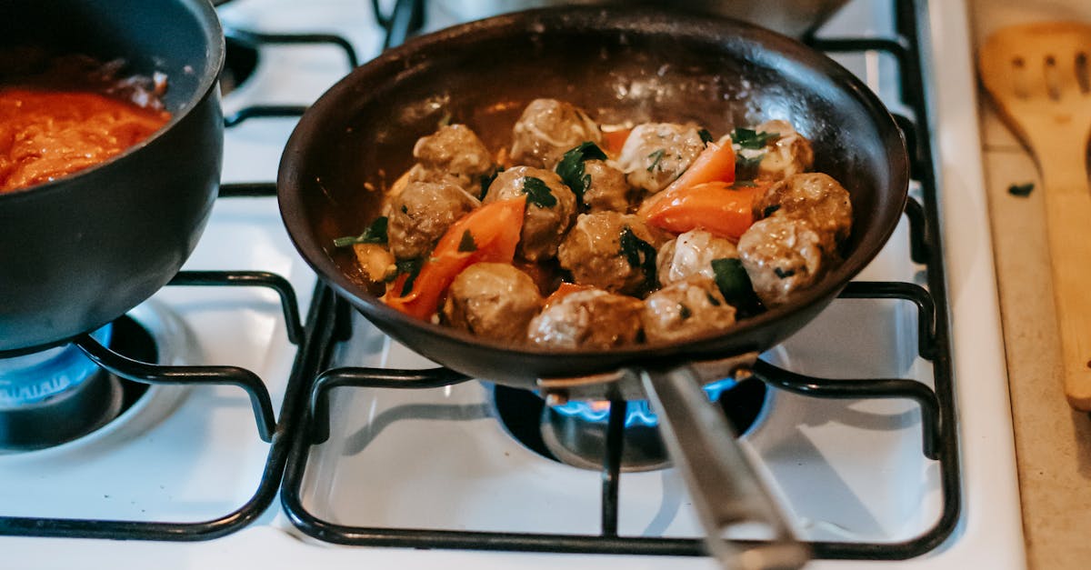 Pan with saucy meatballs frying on gas stove in kitchen