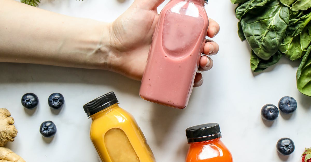 Person Holding Bottle of Smoothie Beside Green Leaves, Carrots and Berries