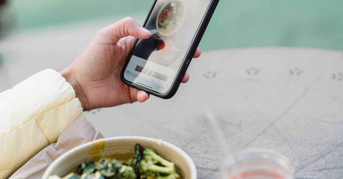 Crop unrecognizable female blogger touching screen on cellphone above street cafe table with healthy food and smoothie