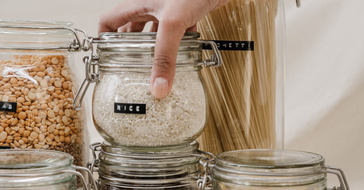 Person Holding Clear Glass Jar With Rice Brown and White Beans